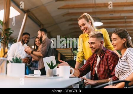 Young colleagues working on laptop and discussing new project Stock Photo