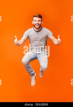 Happy joyful man jumping up in air, demonstrating thumbs up Stock Photo