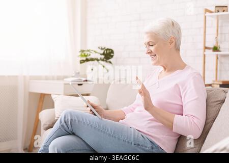 Happy senior woman talking with family via digital tablet Stock Photo