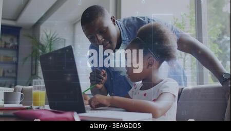 Guiding father in denim leaning over daughter using laptop at dining table holding green pencil Stock Photo