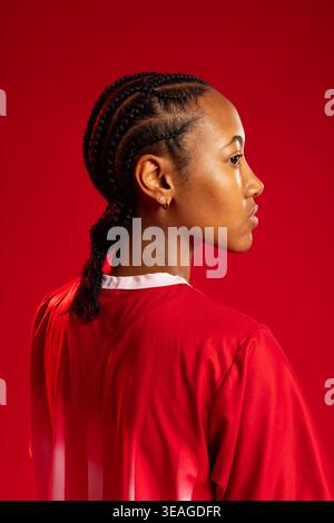 African American woman posing in studio, red jersey white collar showing cornrow braids, gold hoops Stock Photo
