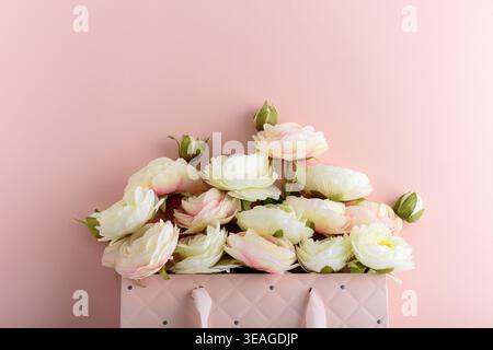 Festive composition featuring a quilted pink gift bag filled with cream and blush artificial rose flowers, accented by a white ribbon bow. Stock Photo