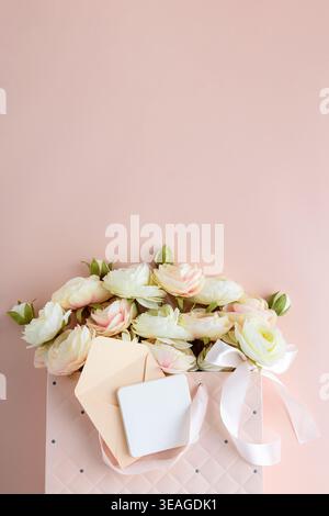 Festive composition featuring a quilted pink gift bag filled with cream and blush artificial rose flowers, accented by a white ribbon bow and gift car Stock Photo