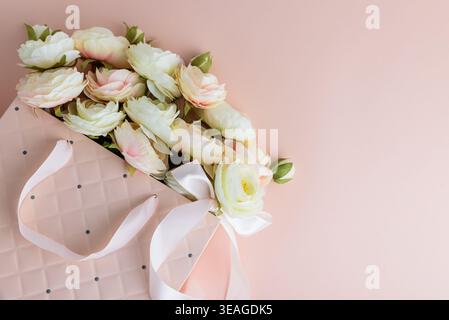 Festive composition featuring a quilted pink gift bag filled with cream and blush artificial rose flowers, accented by a white ribbon bow. Stock Photo