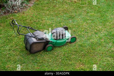 Gasoline lawn mower on freshly cut grass in backyard,garden maintenance equipment for trimming lawn and keeping yard neat and well maintained outdoors Stock Photo