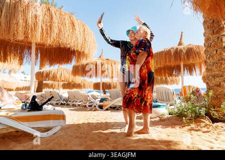 Multigenerational family having fun on tropical beach taking selfie. Mother and daughter on summer vacation at luxury sea resort. Stock Photo
