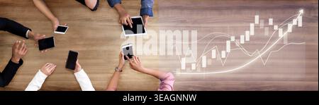 A top-down view of multiple hands interacting with various digital devices on a wooden table, showcasing modern technology role in business analysis a Stock Photo