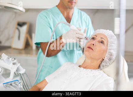 Elderly woman getting facial deep hydration procedure from experienced ...