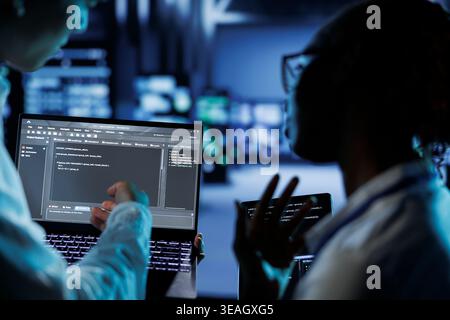 Trained programmers build firewall systems in server room housing advanced infrastructure. Skilled professionals run code on tablet and laptop, to upgrade data center rigs handling demanding workloads Stock Photo