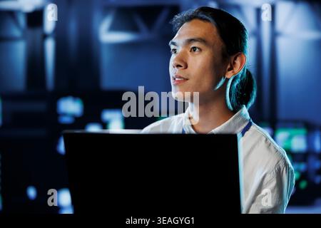 Licensed technician between server hub rows providing processing resources for businesses worldwide. Trained specialist fixing data center mainframes tasked with managing massive databases Stock Photo