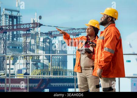 Technicians on offshore platform deck using monitoring app on tablet to track emissions, protecting environment. Coworkers conduct environmental risk assessment for drilling rig using device Stock Photo