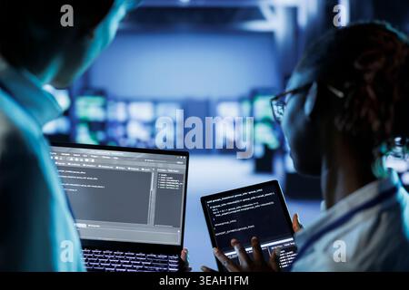 IT developers building firewall systems in server room housing advanced infrastructure. Licensed specialists running code on tablet and laptop, to upgrade data center rigs handling demanding workloads Stock Photo