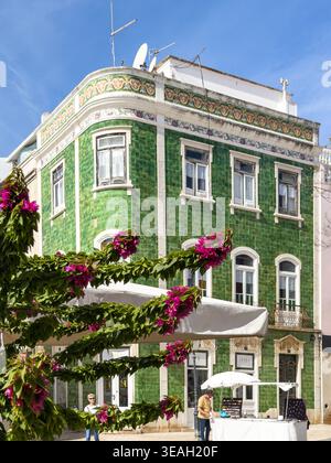 Historic building with green azulejo tiles framed by pink bougainvillea flowers clear blue sky in Luis de Camoes Square lagos Portugal green house Stock Photo