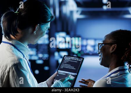 Engineer and african american colleague building firewall systems in server room. Man and woman running code on tablet to upgrade data center rigs handling demanding workloads Stock Photo
