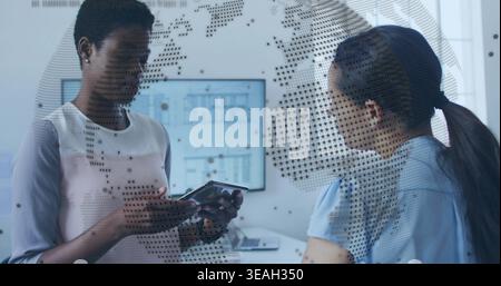 Holding tablet, two colleagues wearing workwear discussing project in office, dotted map on glass Stock Photo