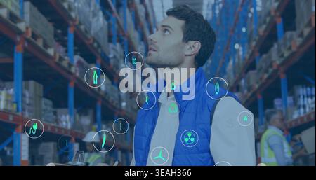 Inspecting supervisor wearing blue vest holding clipboard looking up at warehouse racking, AR icons Stock Photo