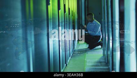 Kneeling tech in blue shirt, dark pants inspecting servers in data center with tablet, copy space Stock Photo