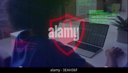 Typing woman wearing blue shirt coding on laptop at home office, with red shield padlock overlay Stock Photo
