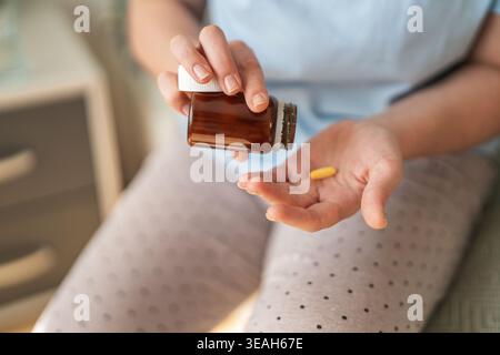 Hands holding a brown medicine bottle and pouring pills into an open palm, illustrating medication use, daily supplements, self-care and treatment at Stock Photo