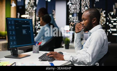 Male black employee focusing on AI virtual assistant usage on monitor, solving problem solving tasks with futuristic tech and machine learning. Communication and IT support. Stock Photo