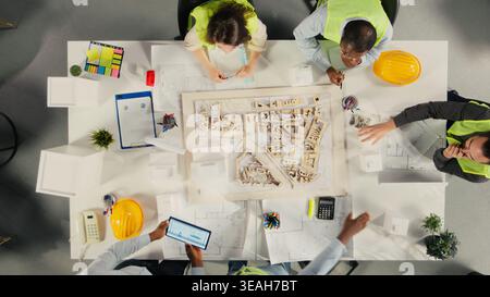 Top down view of real estate developers and architects in office reviewing blueprints and 3D models. Development team discusses urban planning and property investment strategies. Stock Photo