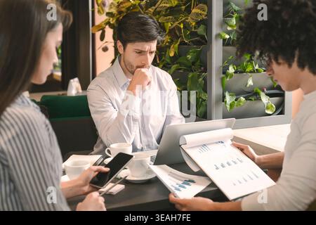 Group of Professionals Analyzing Data and Discussing Strategies in a Modern Cafe Environment Stock Photo
