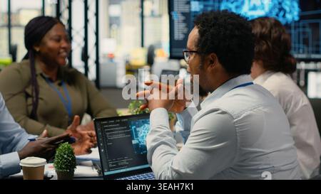 Data scientists in startup office brainstorming leveraging AI tech to gain competitive edge. Coworkers doing meeting to discuss training deep learning predictive models, camera B Stock Photo