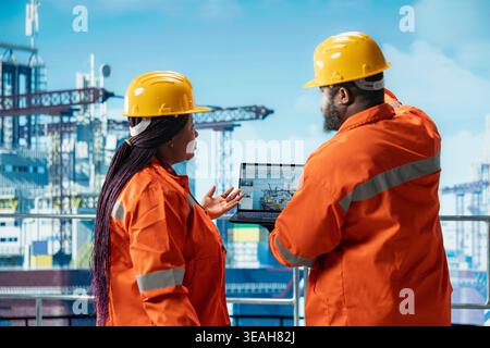 Offshore platform engineers doing brainstorming, using laptop program to monitor equipment metrics. African american drilling barge workers calibrate gear with asset management system on notebook Stock Photo