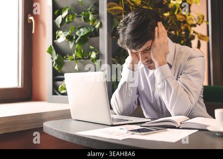 Stressed businessman sitting in front of laptop in cafe Stock Photo