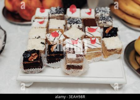 Assorted Petit Layered Cakes On Tray, Variety Of Miniature Cakes With Cream Layers, Chocolate Squares And Red Decorative Accents, Displayed On White Stock Photo
