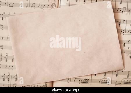 Blank handmade paper sheet placed over music score pages, paper mockup background for invitation, menu or letter design. Music paper composition Stock Photo