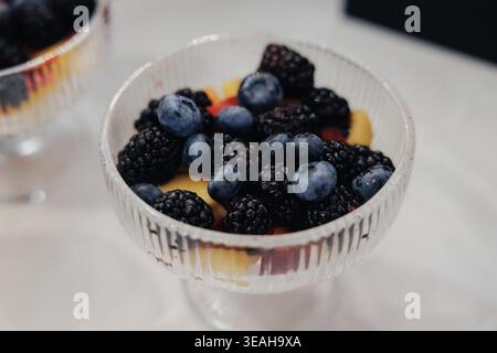 Fresh Blueberries Blackberries In Crystal Bowl, Peach Slices Adding Warm Contrast, Soft Natural Light, Shallow Depth Of Field, Minimalist White Table Stock Photo