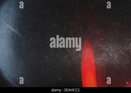 Subtle red light leak on dark grainy and scratched film texture Stock Photo