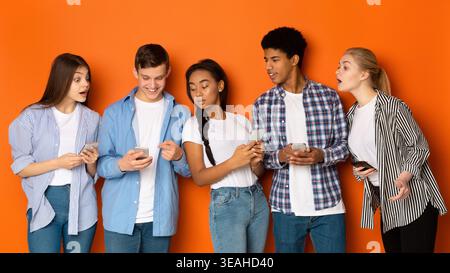 Five Young Individuals Stand Closely Together, Excitedly Discussing Something on Their Smartphones Stock Photo
