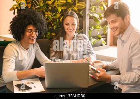 Group Collaborates on Project in Modern Cafe With Greenery During Afternoon Stock Photo