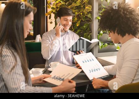 Young man calling to clients, his colleagues studying financial statistics Stock Photo