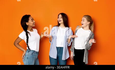 Three Friends Enjoying a Lighthearted Conversation Against a Vibrant Orange Wall Background Stock Photo