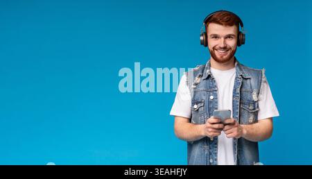 Smiling young man listening to music and holding cellphone on background Stock Photo