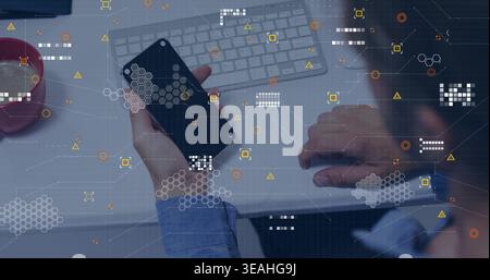 Holding smartphone, man in blue shirt typing on keyboard at desk, wristwatch, red mug, data overlay Stock Photo