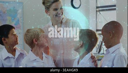Smiling teacher wearing light blouse guiding four kids in white shirts in classroom, hologram globe Stock Photo