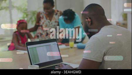 Typing man in gray T-shirt working on laptop at kitchen table, with spreadsheet overlay, copy space Stock Photo