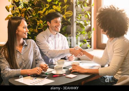 Team Members Discussing Project Ideas During Meeting at Cafe With Indoor Plants Stock Photo