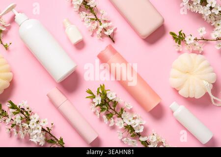 Beautiful blooming spring branches with bottles of shower gels and bath sponge on pink background Stock Photo