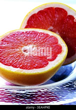 A close-up of two halves of a grapefruit, one whole and one cut in half, on a glass plate. Stock Photo