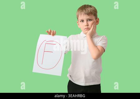 Sad schoolboy holding paper with bad grade on green background Stock Photo