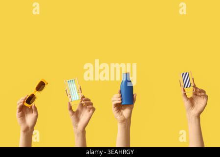 Female hands holding mini deck chairs with sunscreen and sunglasses on yellow background Stock Photo
