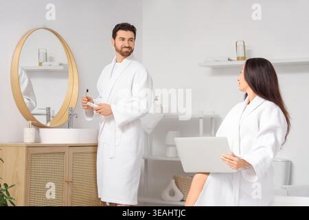 Handsome man brushing teeth while his wife using laptop in bathroom Stock Photo