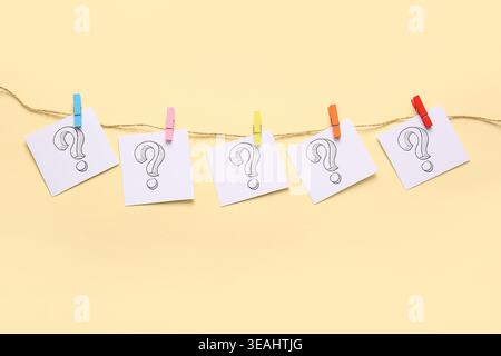 Sticky notes with question marks hanging on rope against color background Stock Photo