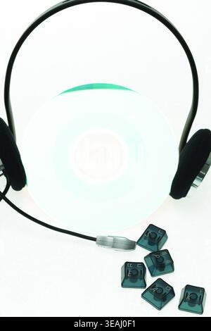 A pair of headphones and several computer keys are placed in front of a CD on a white background. Stock Photo