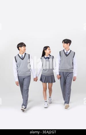 Three students, two boys and one girl, walk together, holding hands, in a school uniform, against a white background. Stock Photo